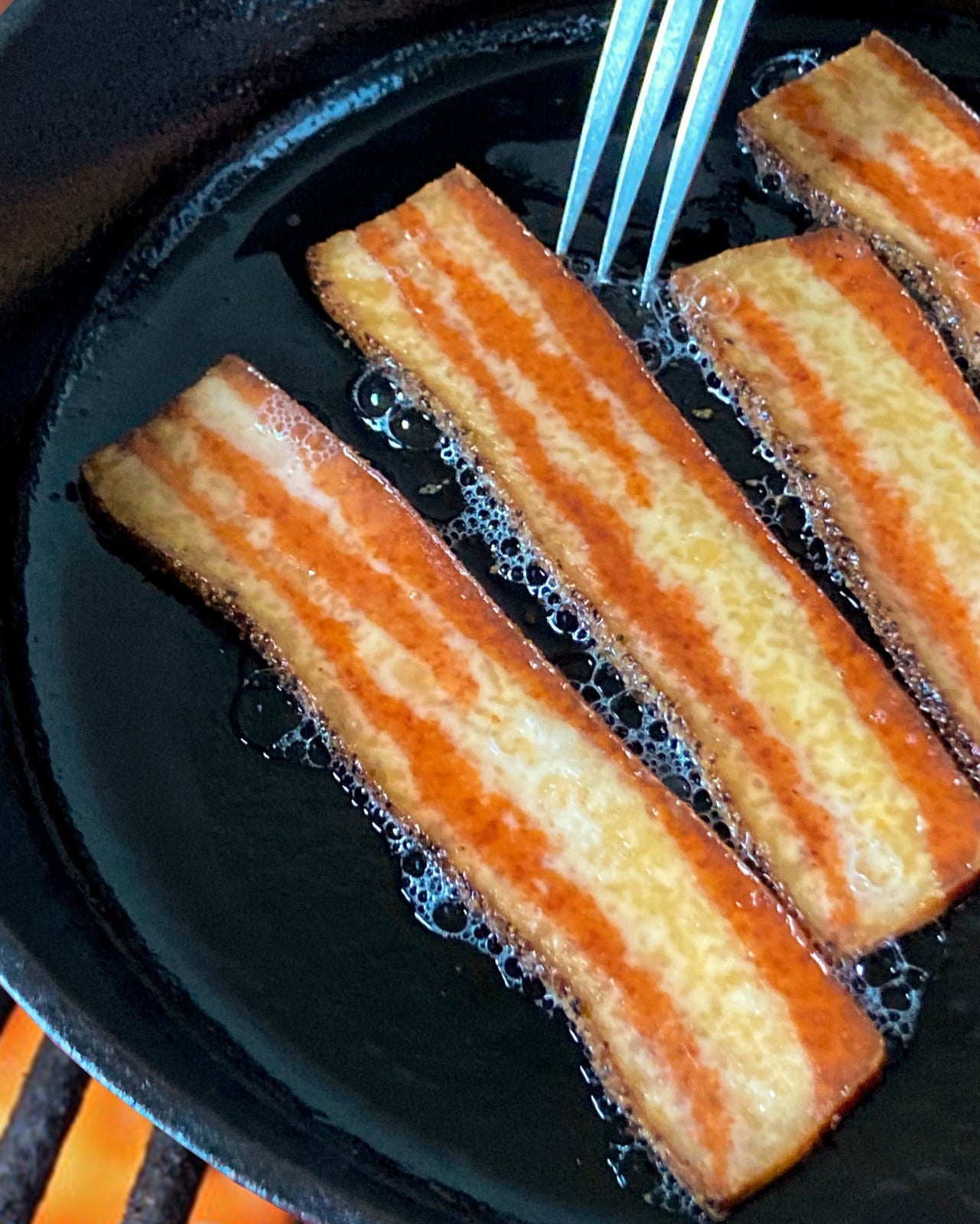 Thrilling Bakon being fried in a cast iron skillet over a fire